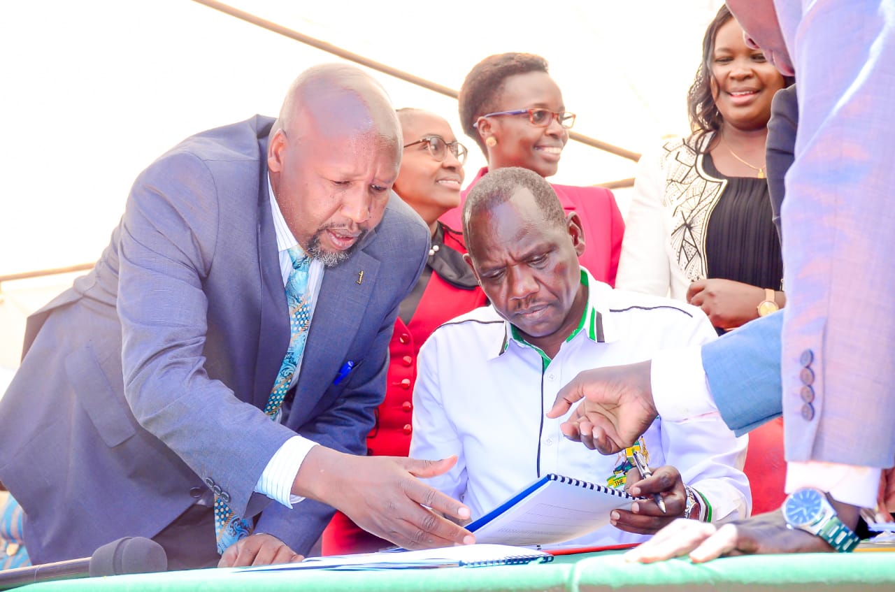 Governor Bii with County Attorney peruses documents that facilitated transfer of the library services and assets to the county.
