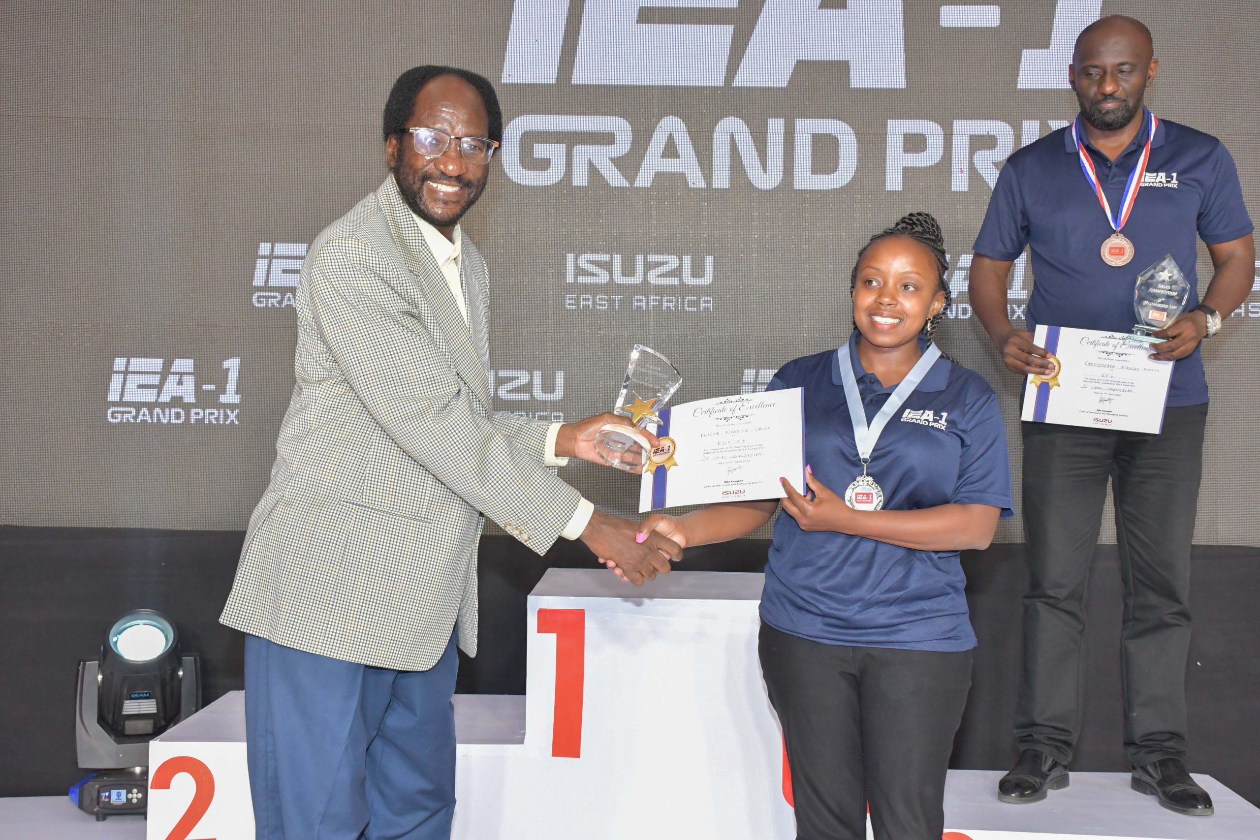 (L-R) Veda Motors Managing Director, David Mwongo, awards RYCE East Africa’s Sales Advisor Fridah Mukami for outstanding performance in the 3S Sales Advisor category as CFG’s Sales Advisor, Christopher Mungai looks on during the 2024 Isuzu East Africa Grand Prix on 17th April 2024.